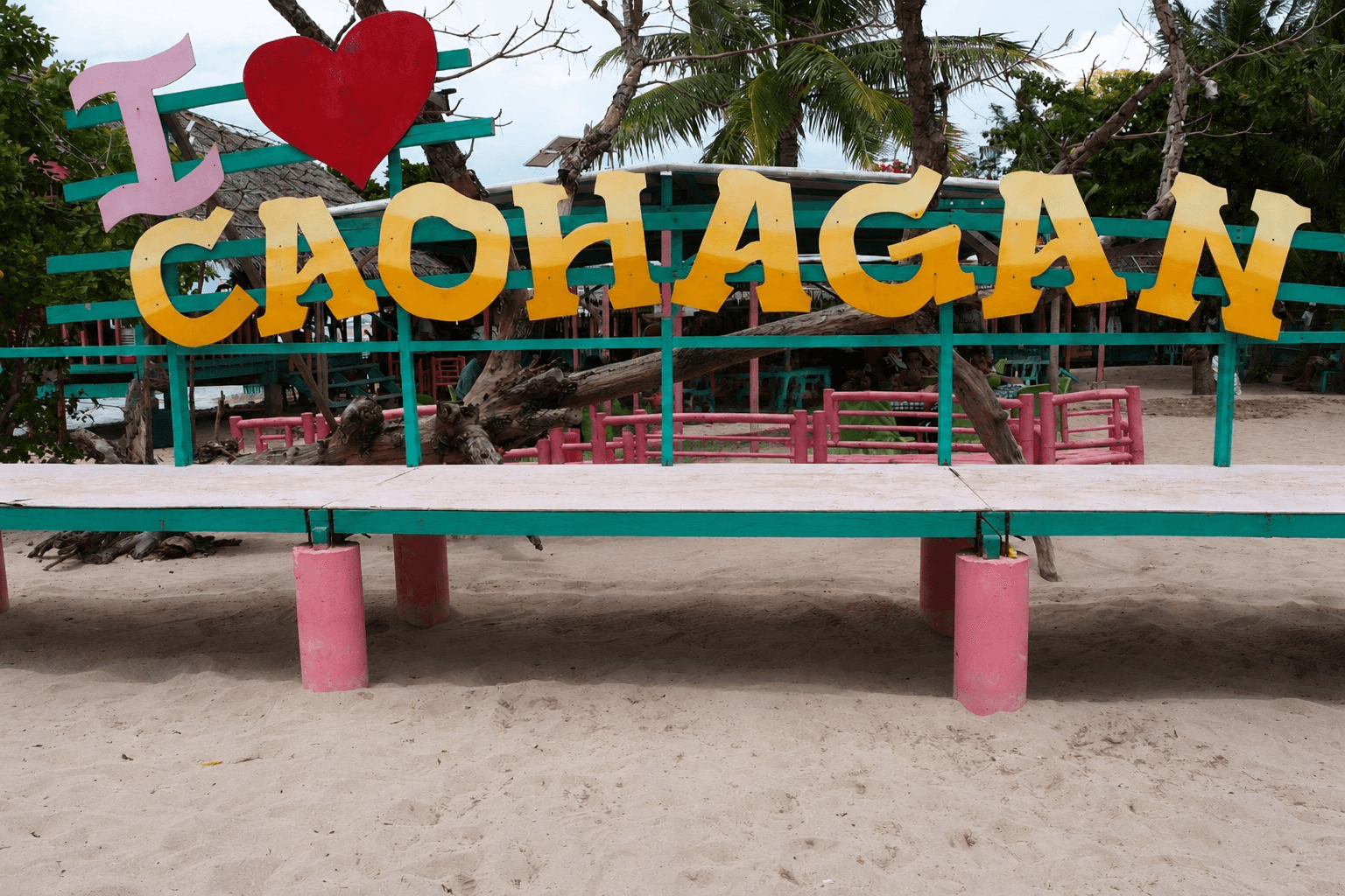 A painted "I love Caohagan" sign standing on the white sand in front of the island's open-sided eating shelters