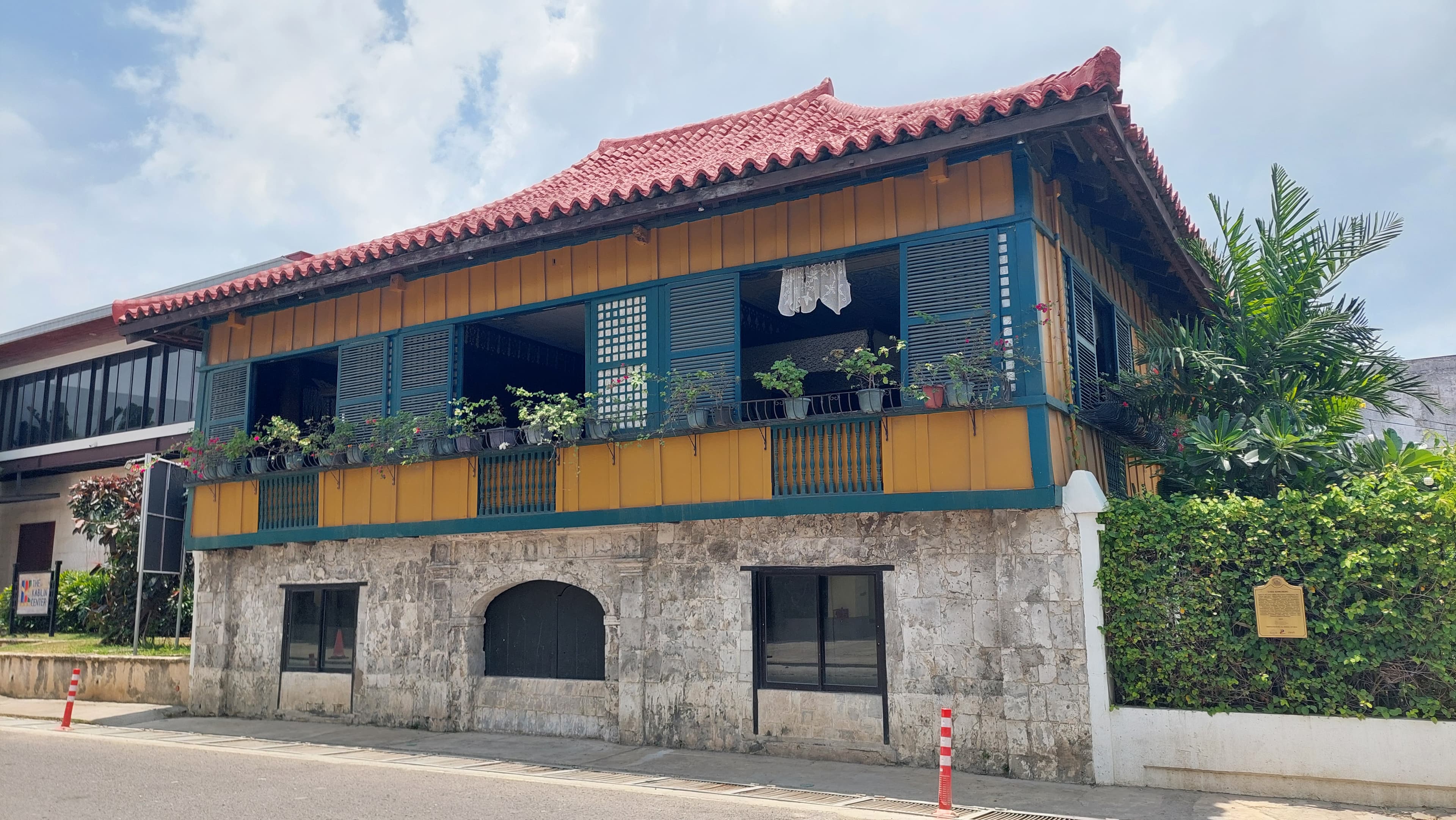 The museum's yellow and teal timber upper storey under a red tile roof, set on coral-stone walls, with potted plants ranged along the balcony rail