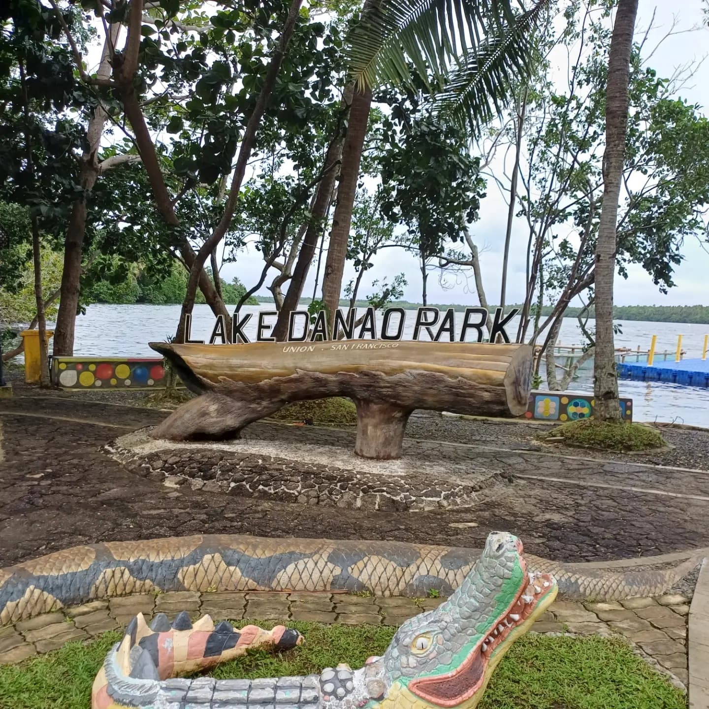 The Lake Danao Park entrance sign mounted on a carved log, with the lake and a floating pontoon behind the trees