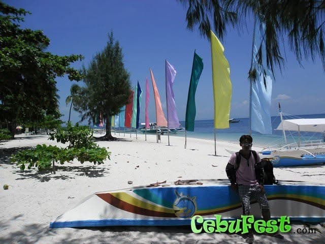 A row of tall coloured banners along a white sand beach on Malapascua, with an outrigger boat drawn up on the sand